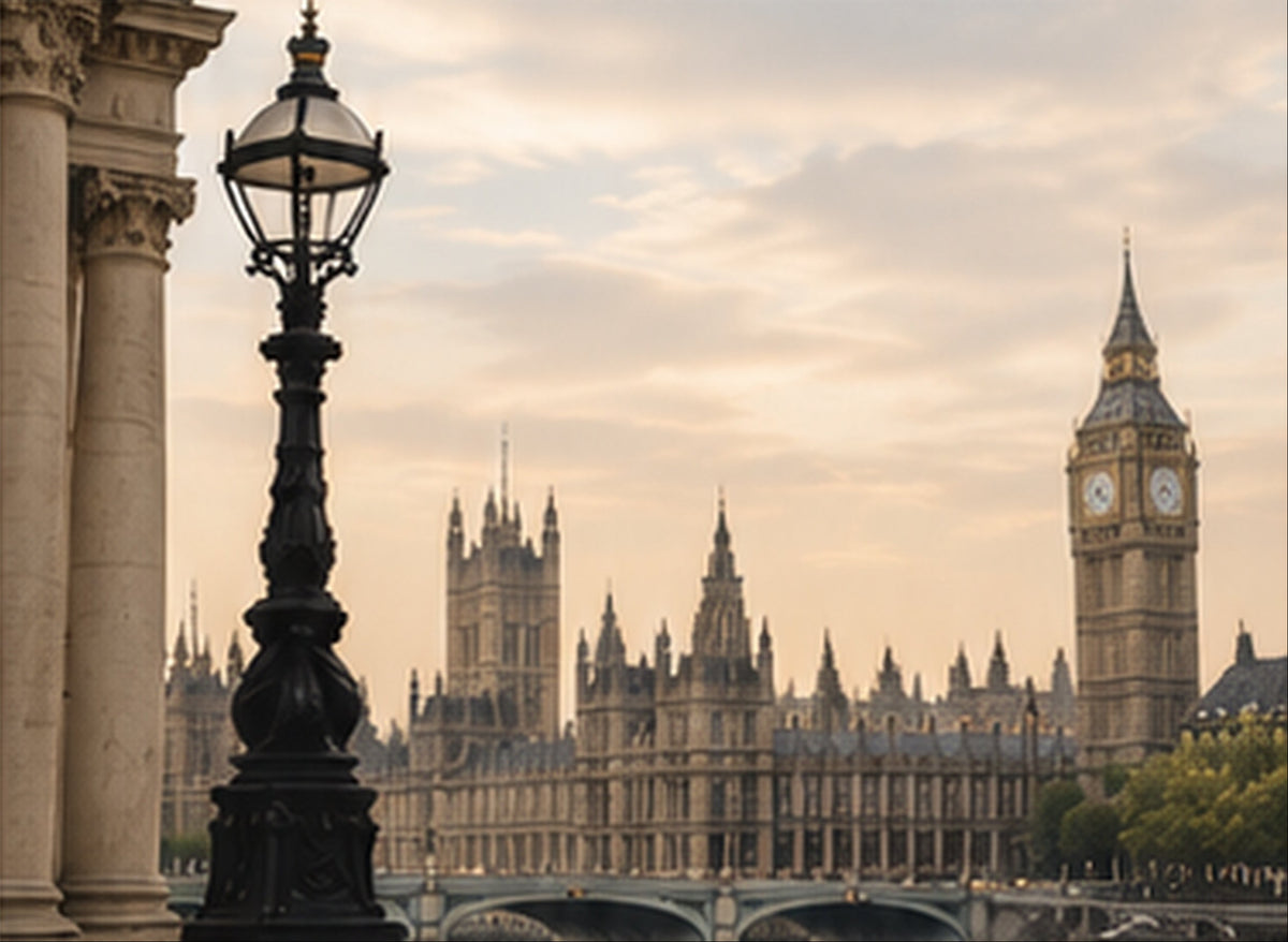 A scenic photograph of London featuring Big Ben and the Palace of Westminster in the distance, with a black ornate street lamp in the foreground against a warm cloudy sky.