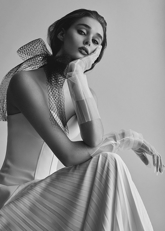 Model wears strapless bustier crepe pleated wedding dress with  tulle opera gloves and bow at neck