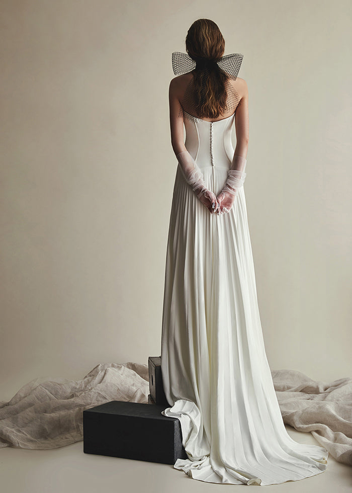 Model stands tall wearing pleated crepe a-line wedding dress tulle gloves and cage veil bow