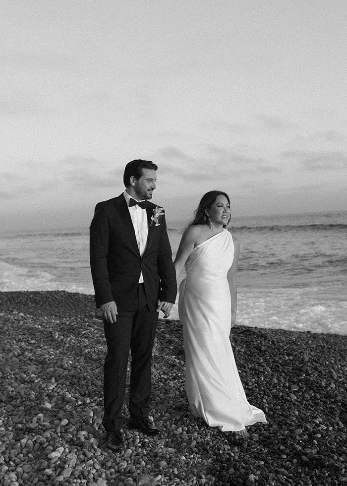 Bride stands tall on the beach wearing one shoulder stretch satin cowl back wedding dress