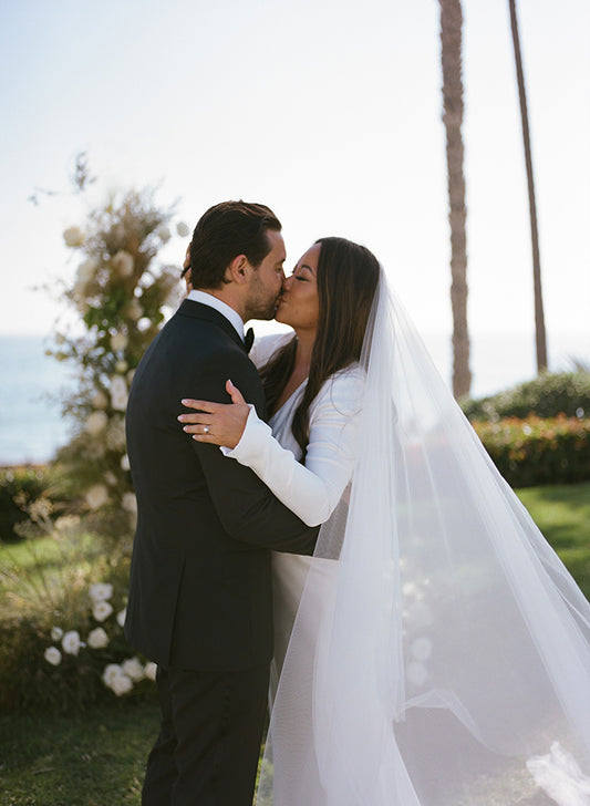 Bride kisses groom wearing silk cathedral veil and silk long sleeve wedding dress